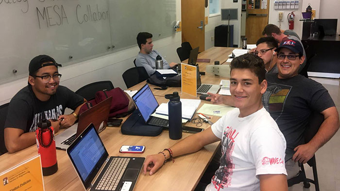 Group of first-year engineering students studying together in the MESA center with laptops and shared resources.