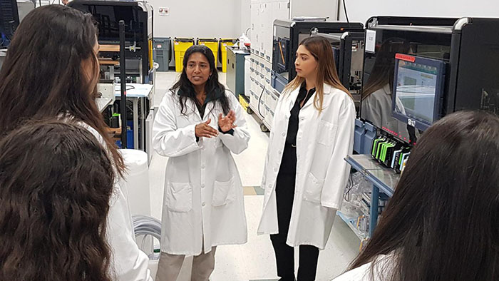 Engineering students in lab coats touring a research facility and engaging in hands-on career exploration.