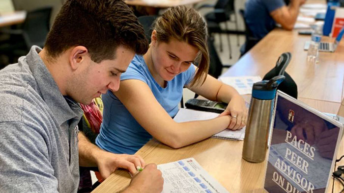 Student peer advisor guiding another student through academic resources and planning at a shared table.