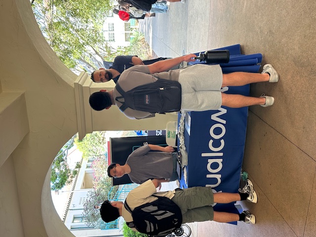 Two representatives from Qualcomm talk to 2 students at an outdoors tabling event.