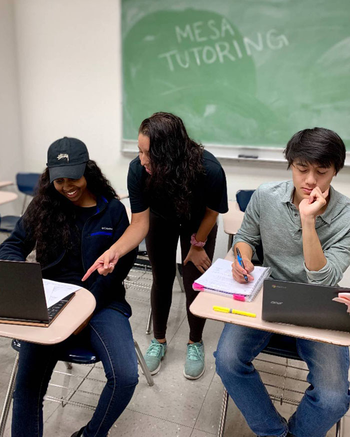 Students engaged in MESA tutoring session with laptops and notes in a collaborative classroom setting.
